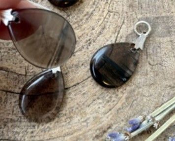 Vier druppelvormige, gepolijste, donkerbruine hangers met zilveren oogjes op een houten oppervlak.