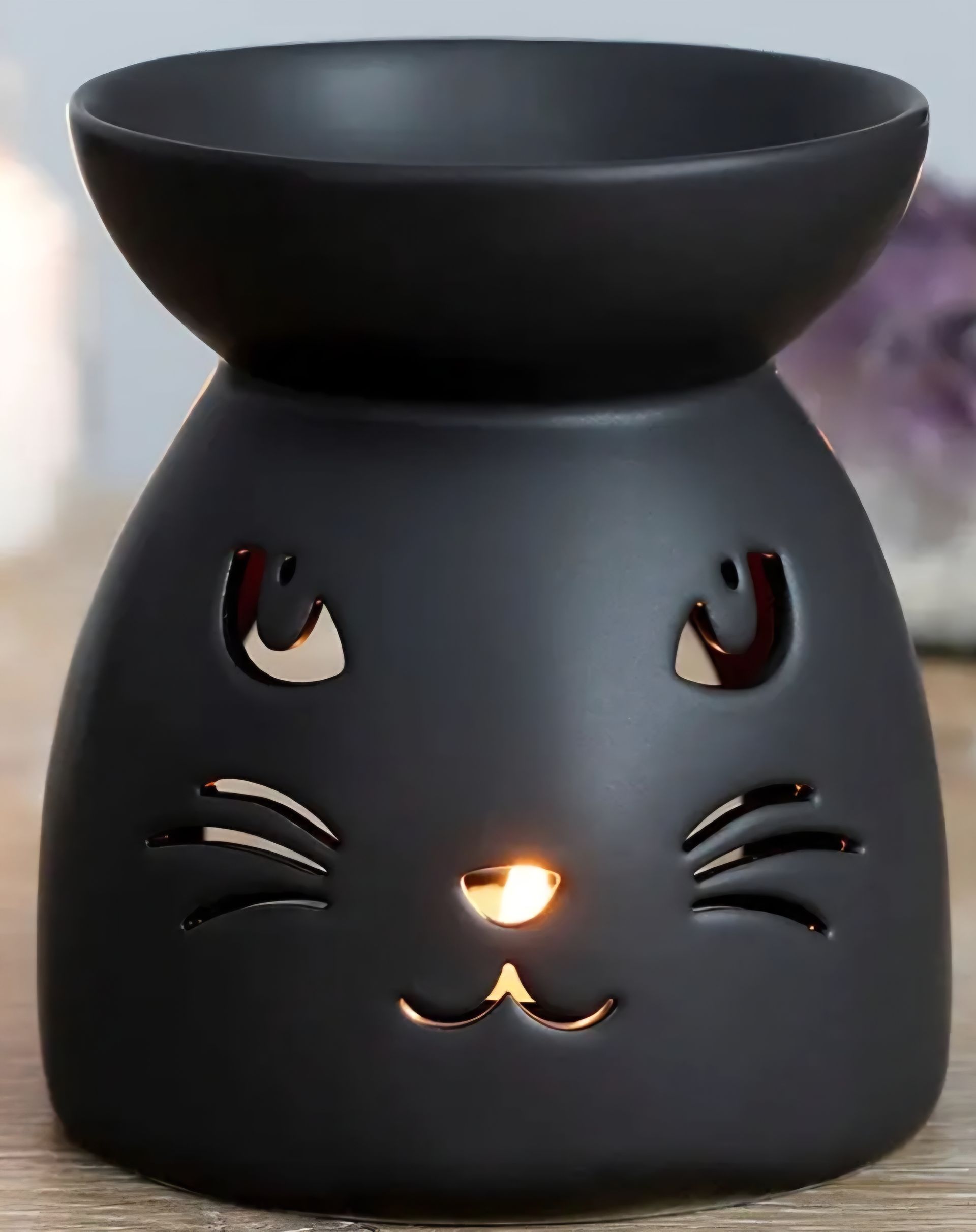 Zwarte oliebrander in de vorm van een kat. met een heksenhoed, tegen een griezelige blauwe achtergrond.