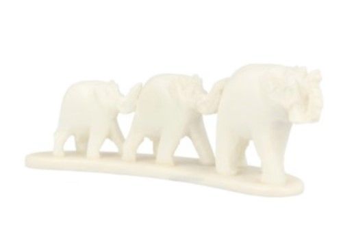 Ivoorkleurig beeldhouwwerk van een olifantenfamilie op een houten ondergrond met groen op de achtergrond.