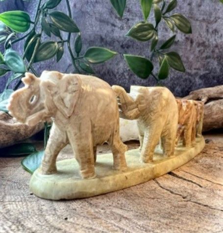 Vier gebeeldhouwde stenen olifanten die op een rij lopen, in verschillende tinten beige en bruin.