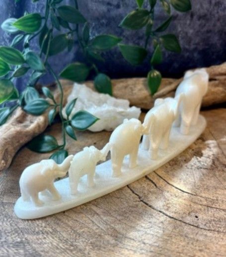 Ivoorkleurige, gesneden olifanten op een rij, van slurf tot staart, op een gebogen voetstuk.