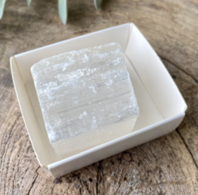 Vierkant selenietkristal in een vierkant, gebroken wit schaaltje, op een witte achtergrond.