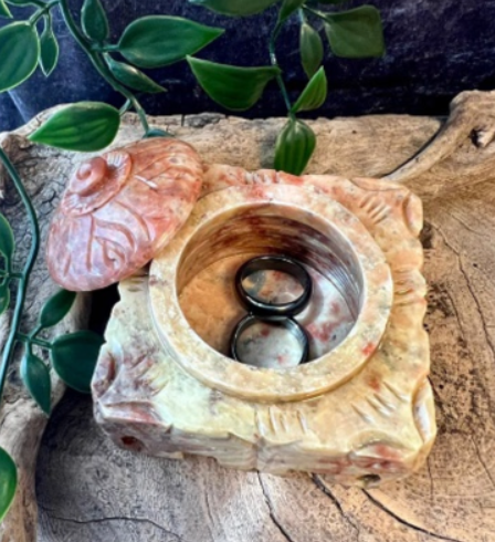 Gesneden stenen doos, lichtbeige met rode aders, met een koepelvormig deksel. Aan de zijkanten zijn olifanten gegraveerd.