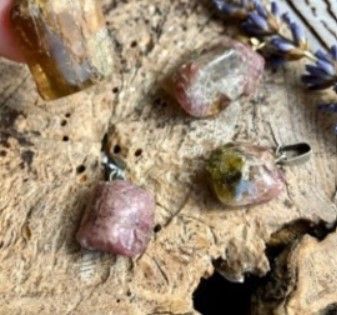 Close-up van vier veelkleurige edelsteenhangers op een getextureerd houten oppervlak met lavendeltakjes.