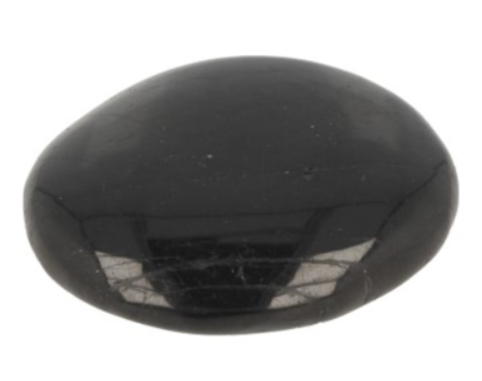 Drie gepolijste zwarte toermalijnstenen op hout met groene bladeren.