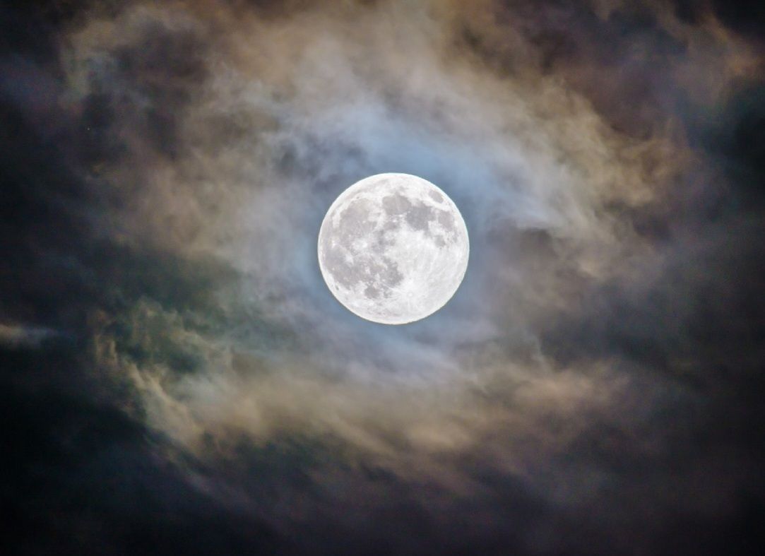 De volle maan schijnt helder door de donkere, veelkleurige wolken.