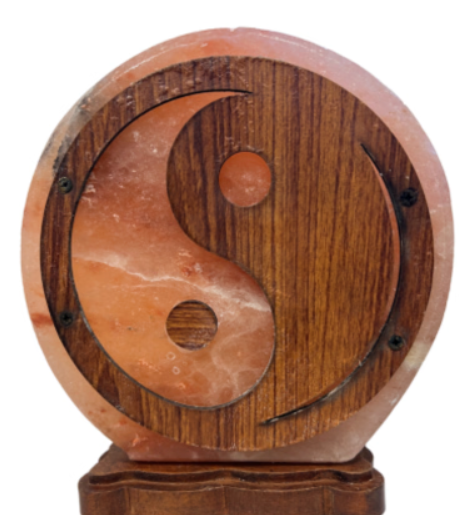 Gloeiende roze zoutlamp met een houten yin-yang symbool op een houten voet.