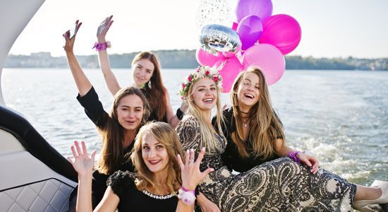 a group of women are sitting on a boat holding balloons .