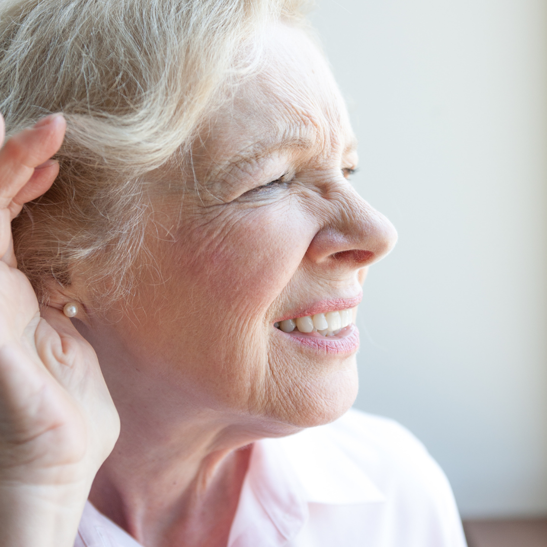 A woman is smiling and holding her hand to her ear