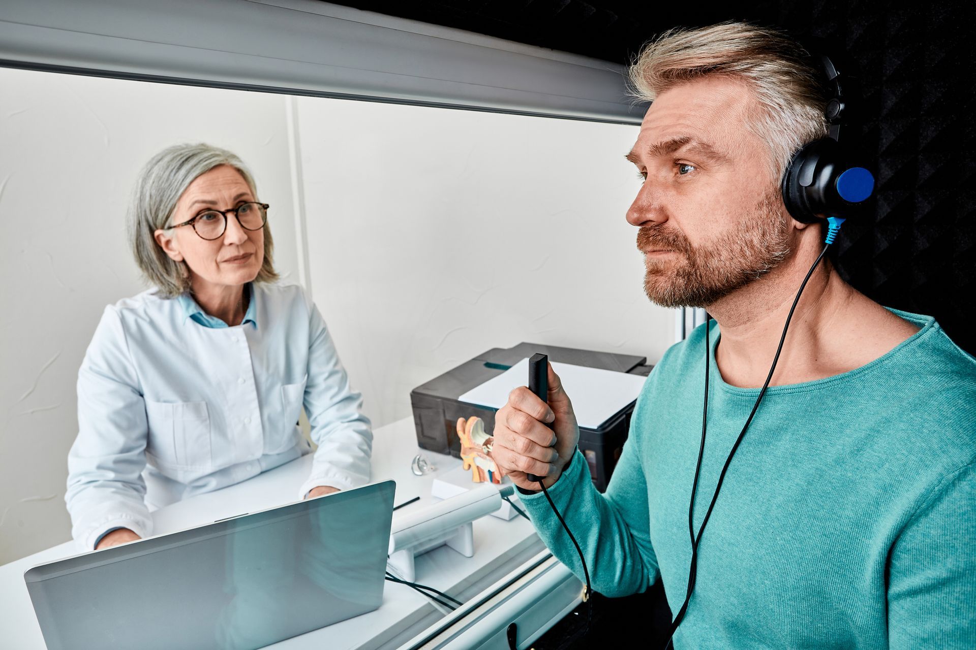 Man in soundproof booth undergoing hearing test with audiologist.