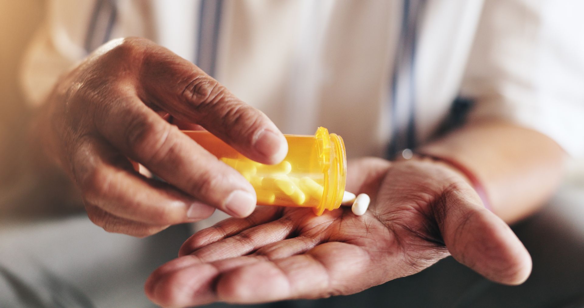 Person pouring pills from an orange prescription bottle into their open palm.