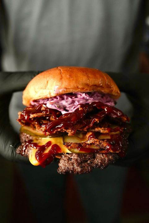 A person wearing black gloves is holding a hamburger on a plate.