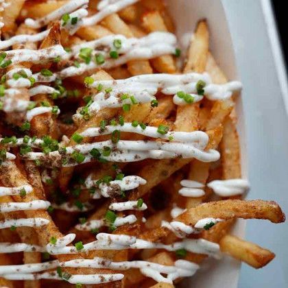 A close up of a plate of french fries with white sauce and green onions.