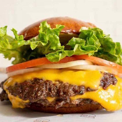 A cheeseburger with lettuce , tomatoes , onions and pickles on a bun.