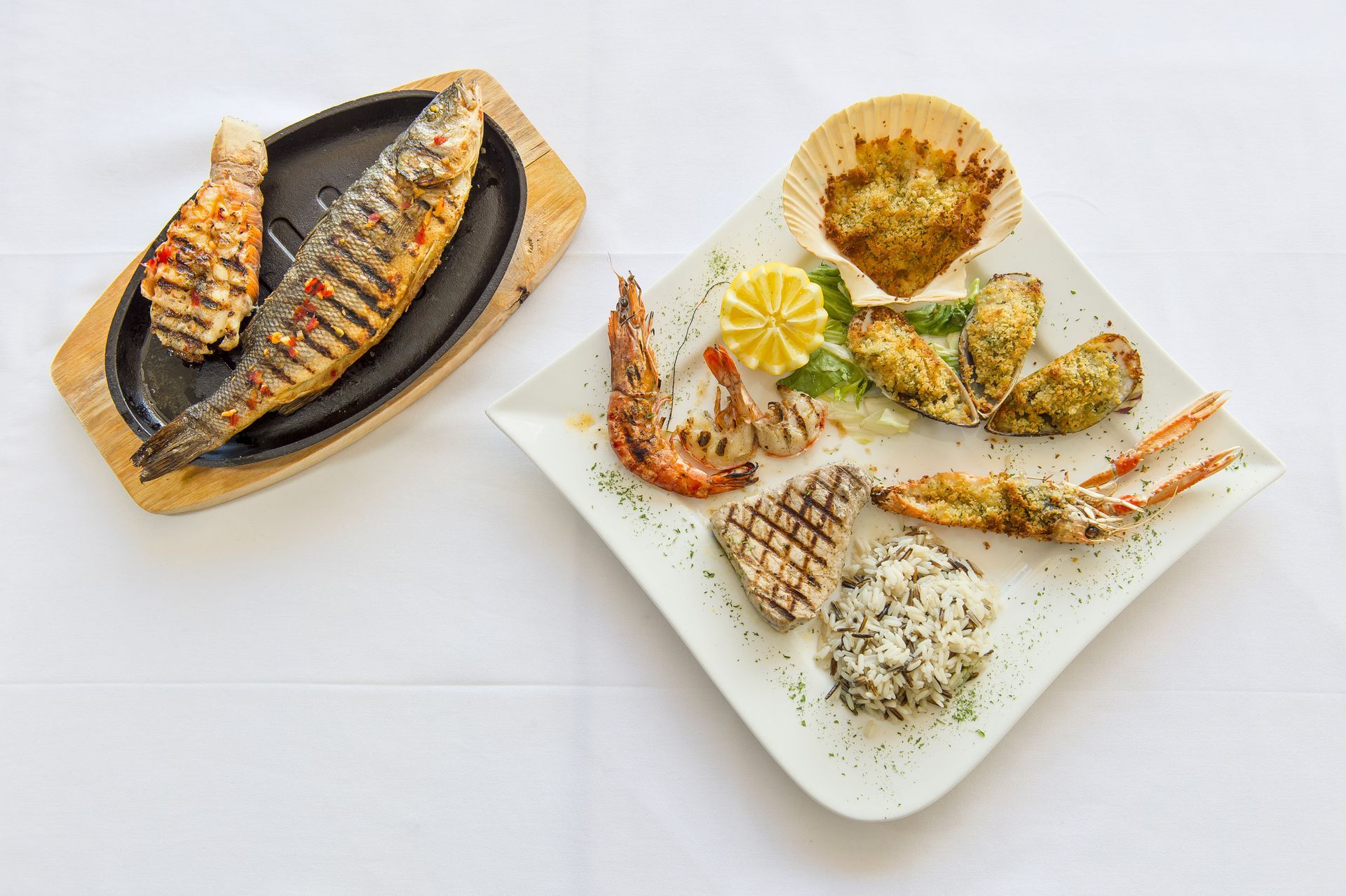 Un piatto di cibo con sopra un pesce e gamberetti su un tavolo.