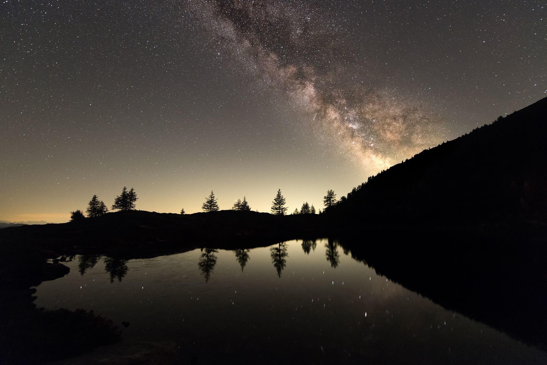 Un cielo notturno stellato sopra un lago con alberi in primo piano