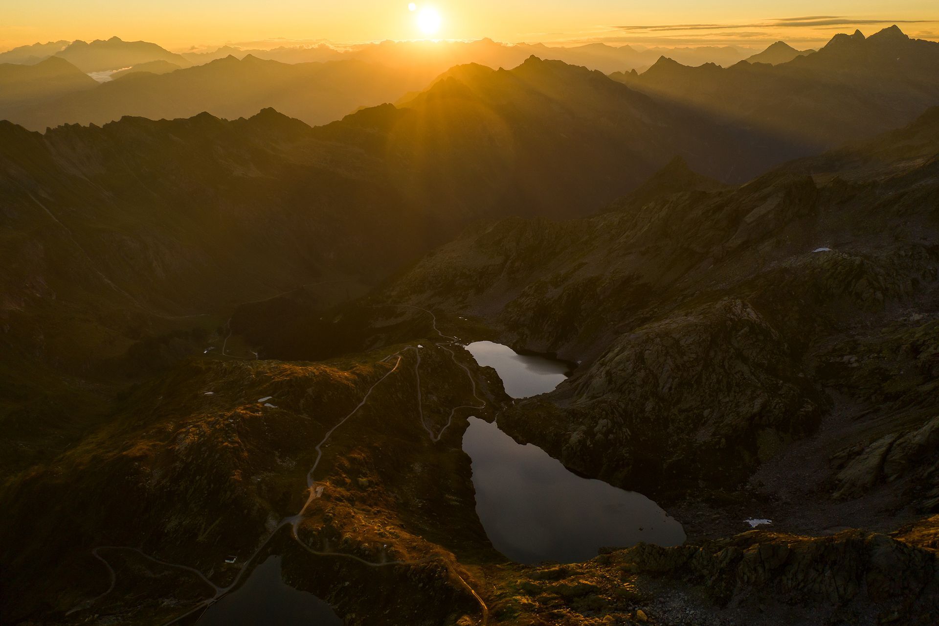 Il sole sta tramontando su una catena montuosa con un lago in primo piano.