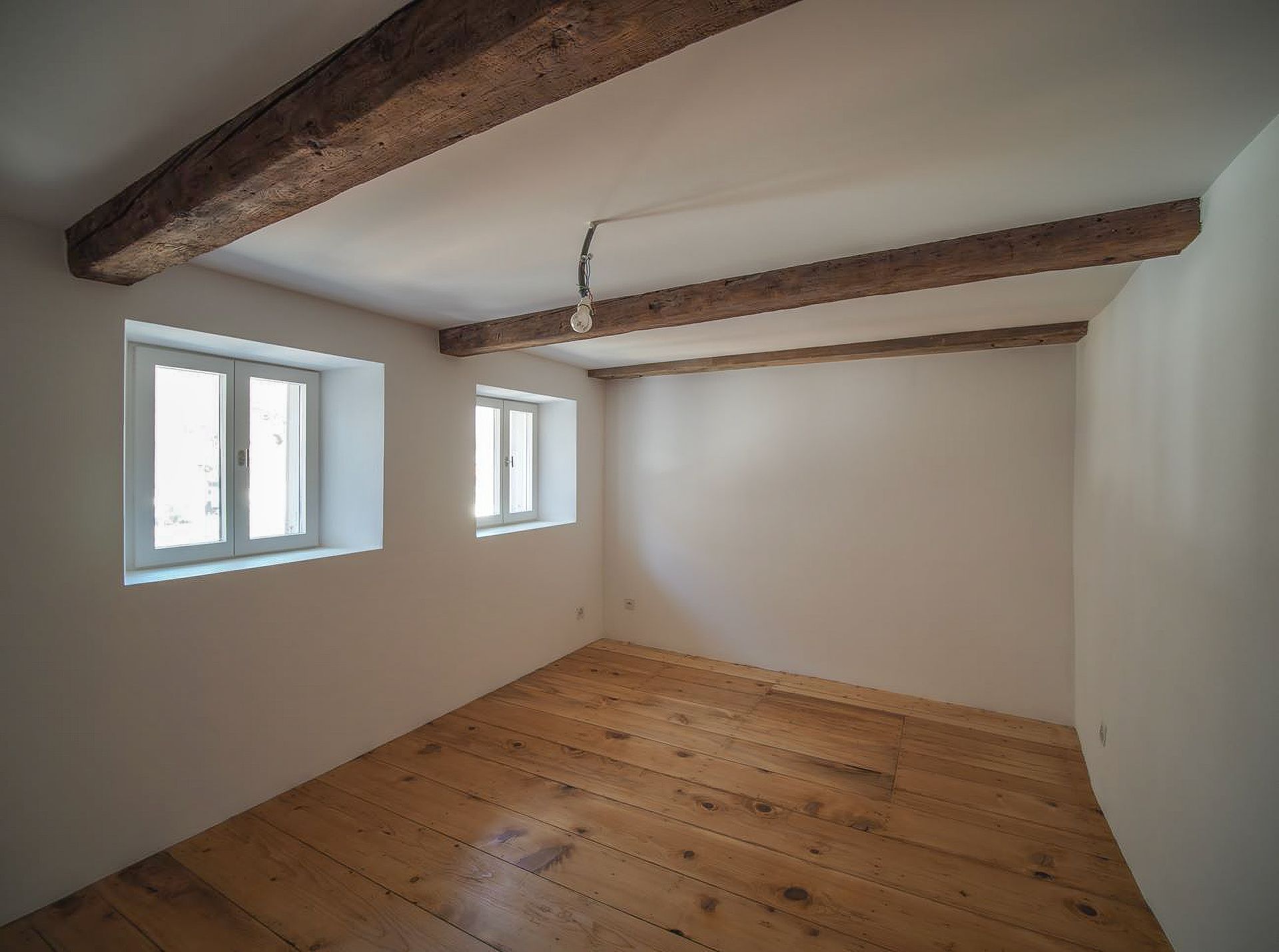 Una stanza vuota con pavimenti in legno e due finestre.