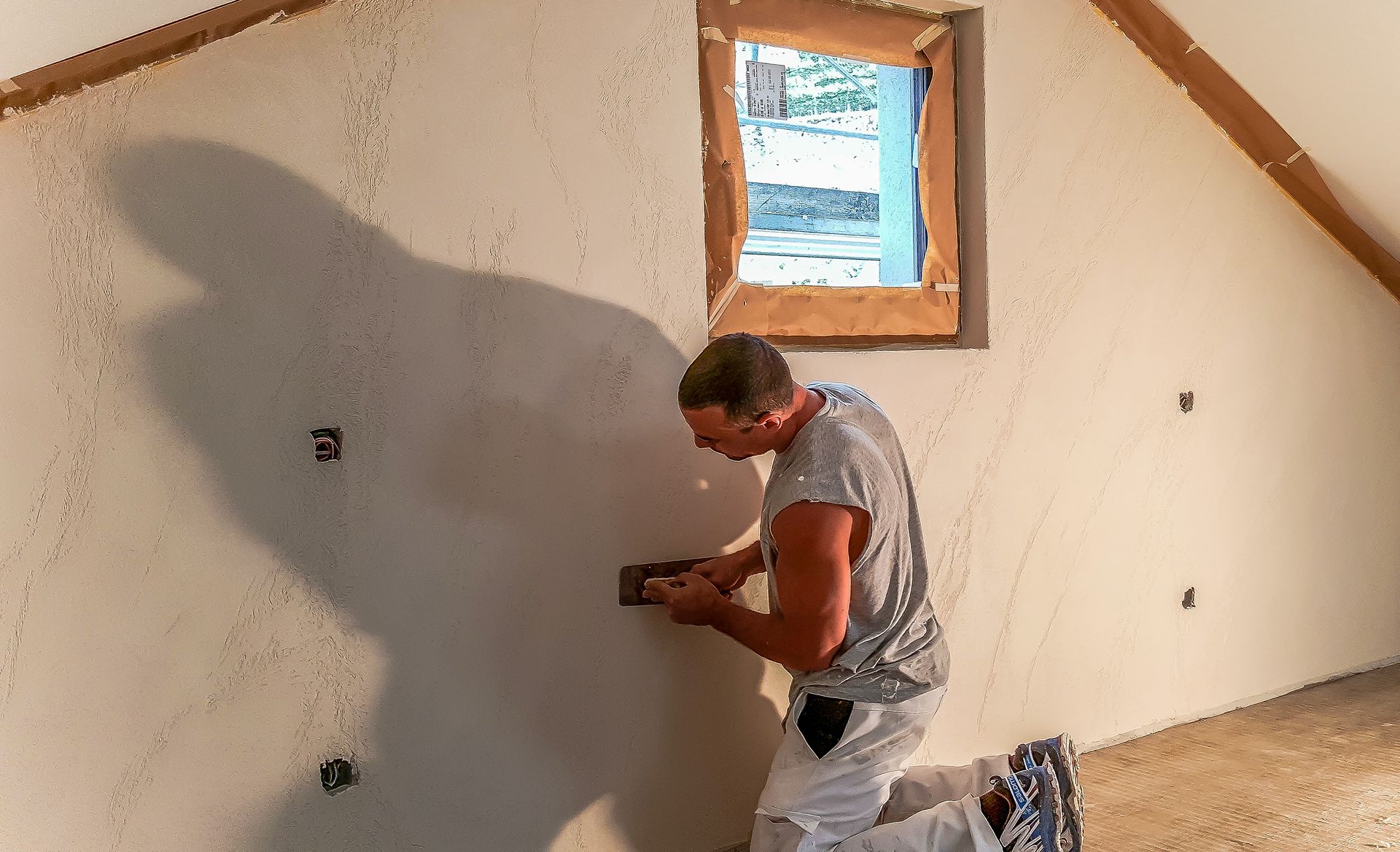 Un uomo sta lavorando su un muro in una stanza con una finestra.