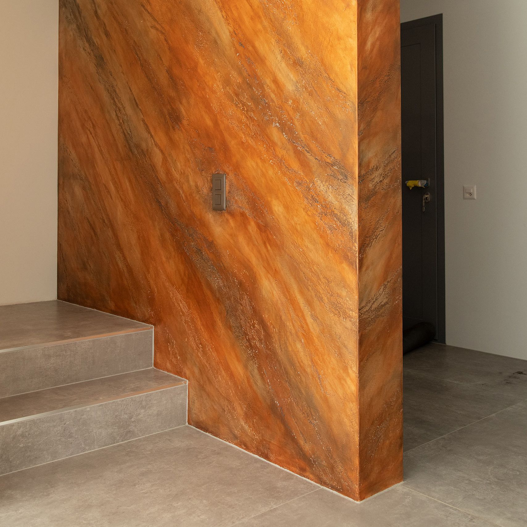 Un angolo di una stanza con un muro in stucco marrone e scale