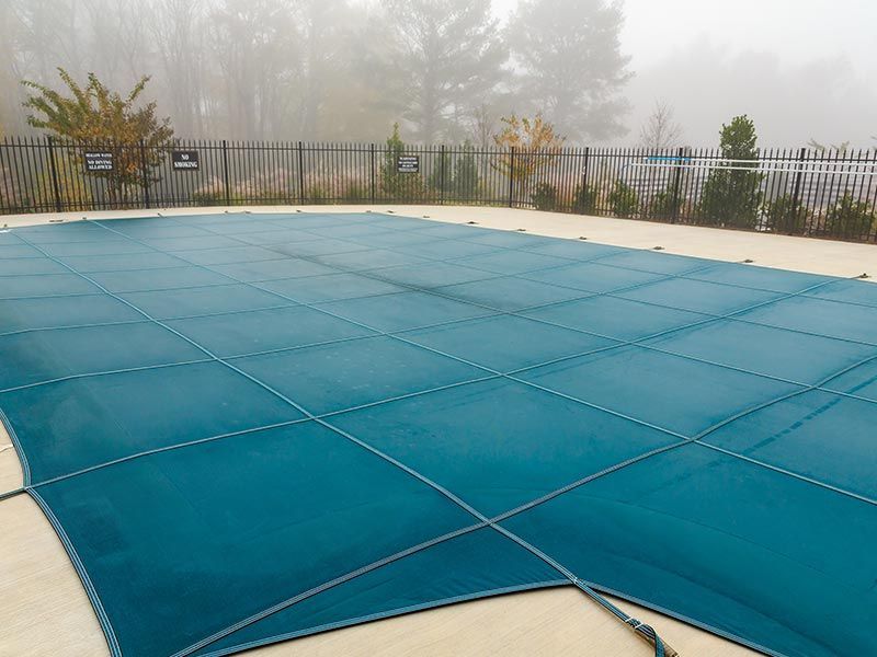 Blue pool cover on an outdoor pool, bordered by a fence in a foggy setting.