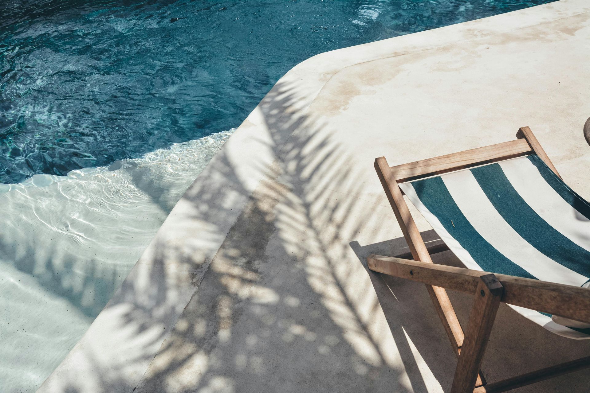 Striped deck chair by a pool, palm shadow on stone.