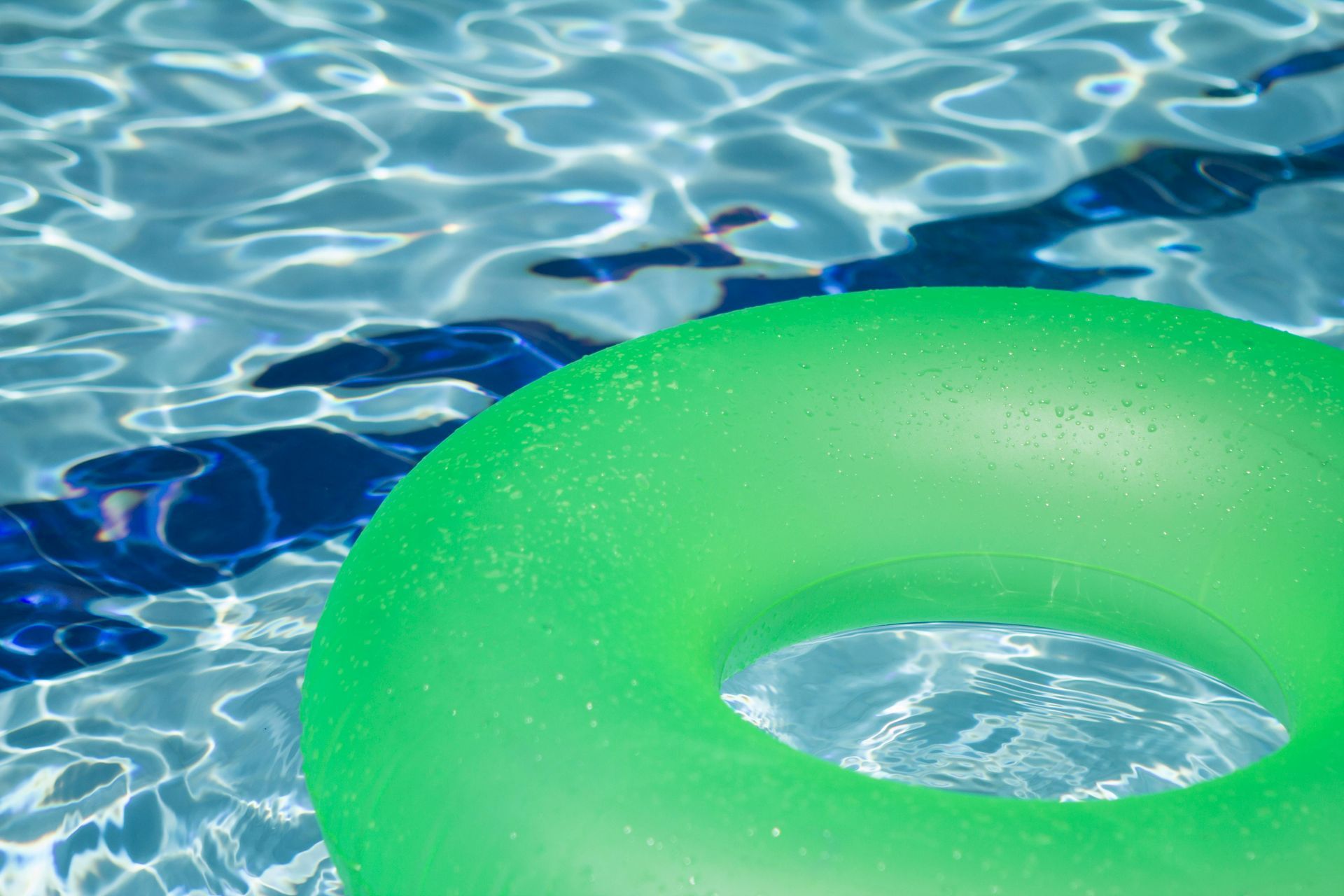 Green inflatable tube floating in a clear blue swimming pool.