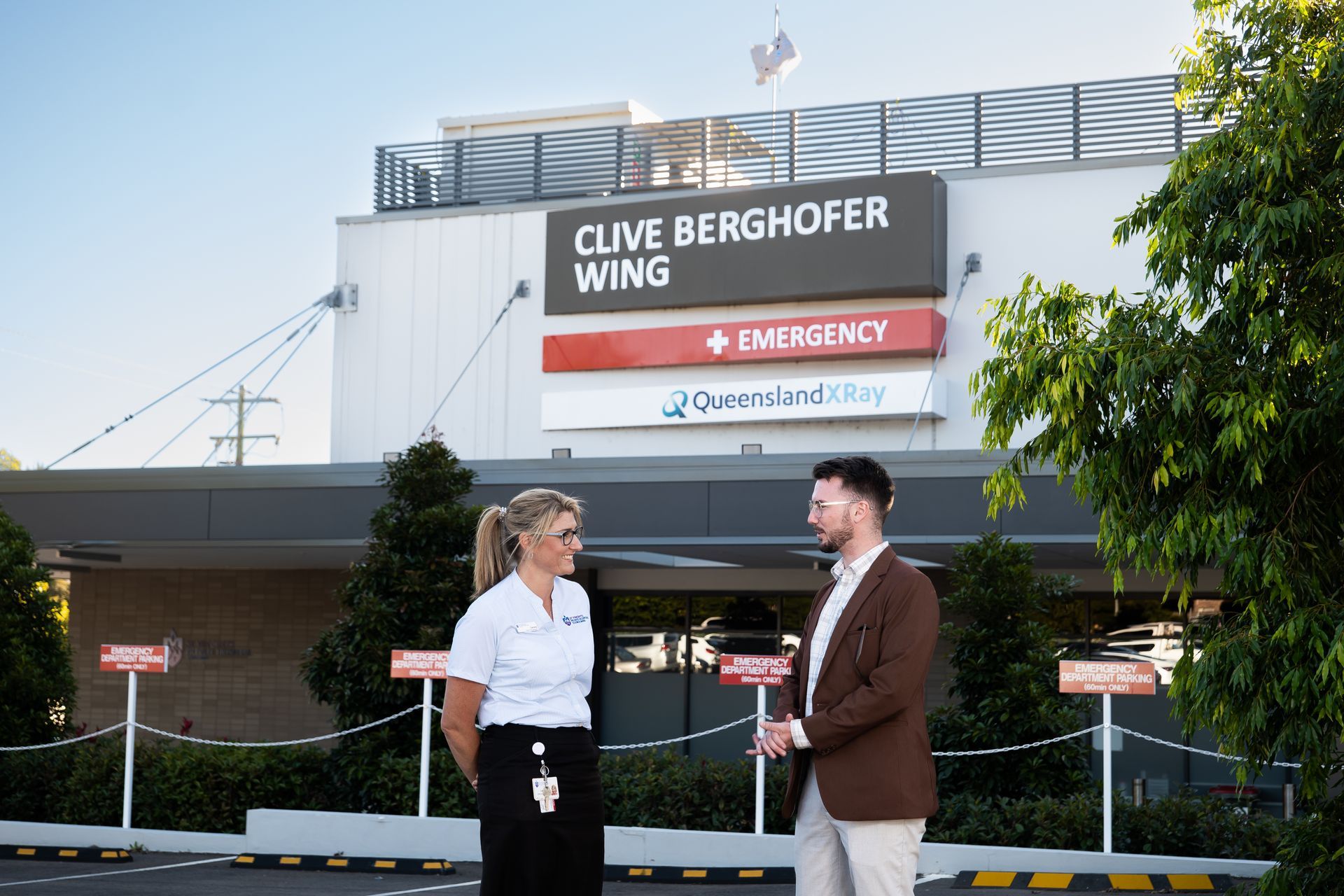 a man and a woman are standing in front of a building that says clive berghofer wing based in Toowoomba
