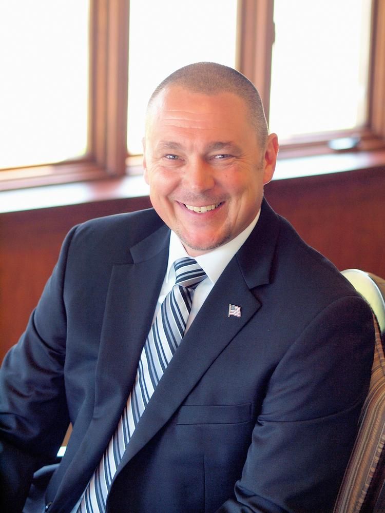 A man in a suit and tie is smiling while sitting in front of a window.