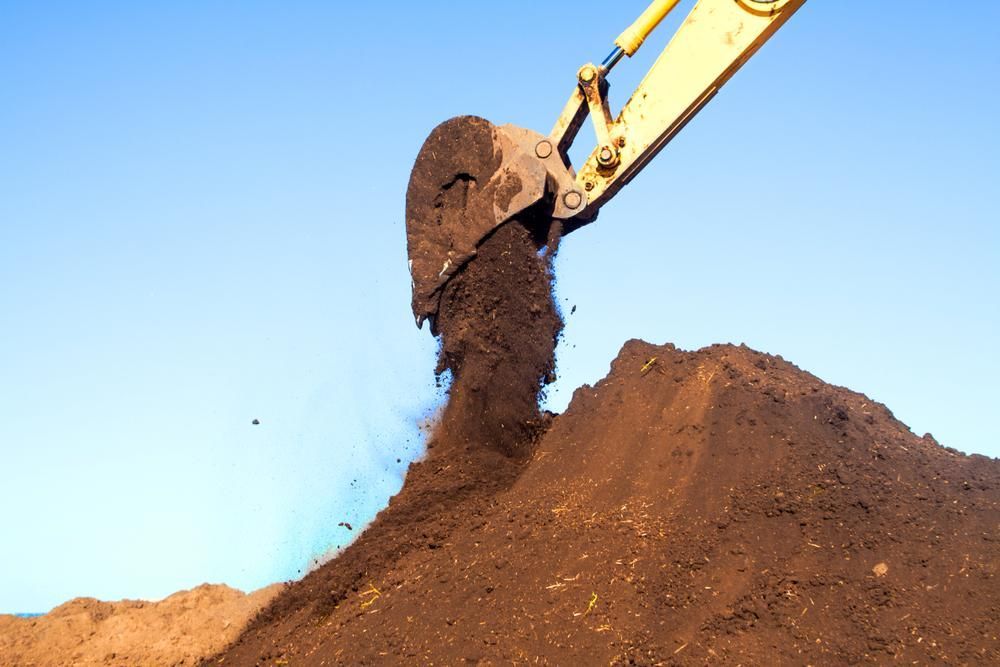 A Large Pile Of Dirt Is Being Scooped Up By An Excavator — Glen Tier Bobcat & Truck Hire In Woree, QLD