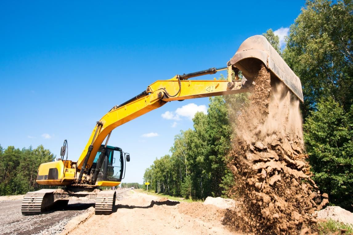 A Yellow Excavator Is Loading Dirt Into A Bucket On A Construction Site — Glen Tier Bobcat & Truck Hire In Woree, QLD