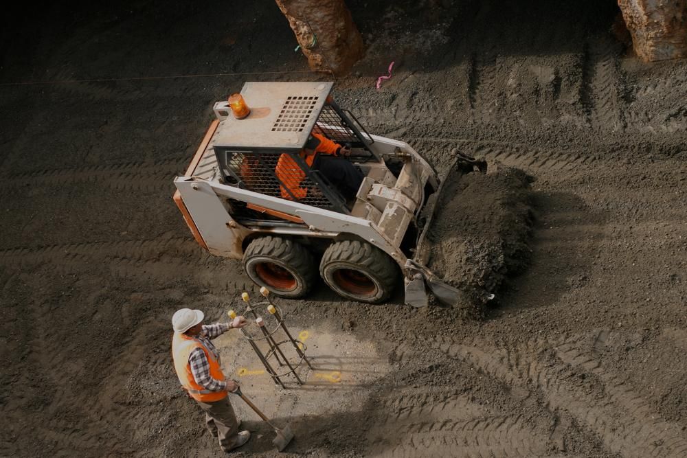 A Man Is Standing Next To A Bulldozer On A Dirt Road — Glen Tier Bobcat & Truck Hire In Woree, QLD