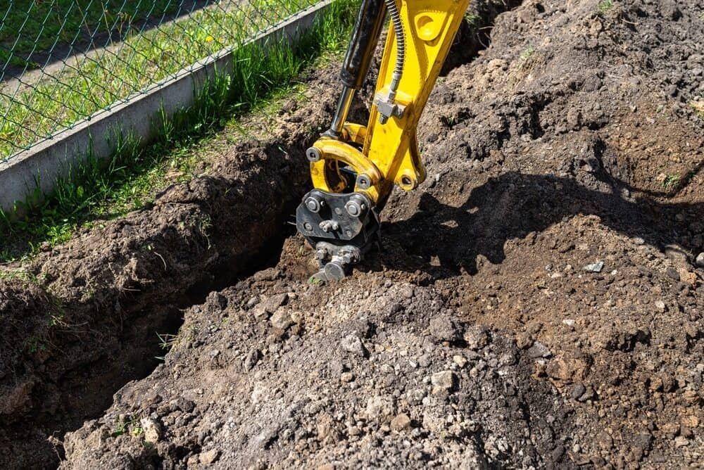 A Yellow Excavator Is Digging A Hole In The Ground — Glen Tier Bobcat & Truck Hire In Innisfail, QLD