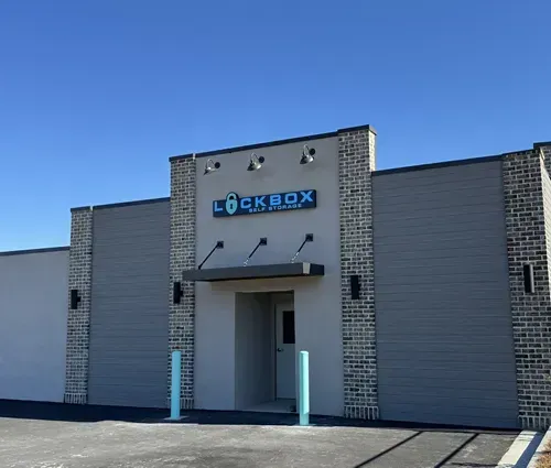 Storage units with yellow doors and gray siding against a blue sky with fluffy clouds.