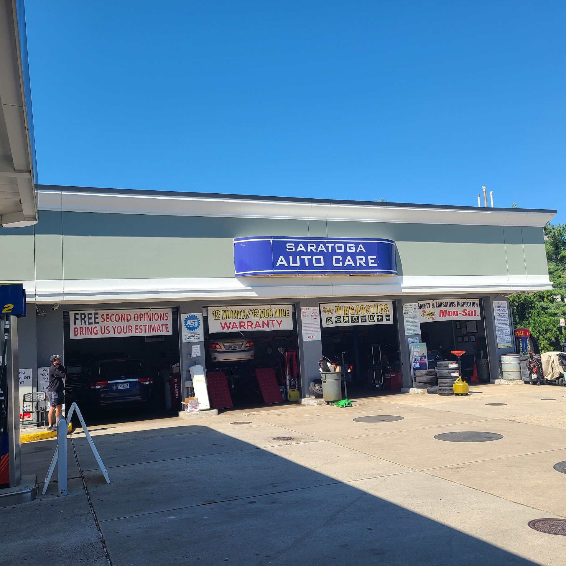 Saratoga Auto Care, blue sign over gray building with service bays. Cars in bays, blue sky. | Saratoga Sunoco