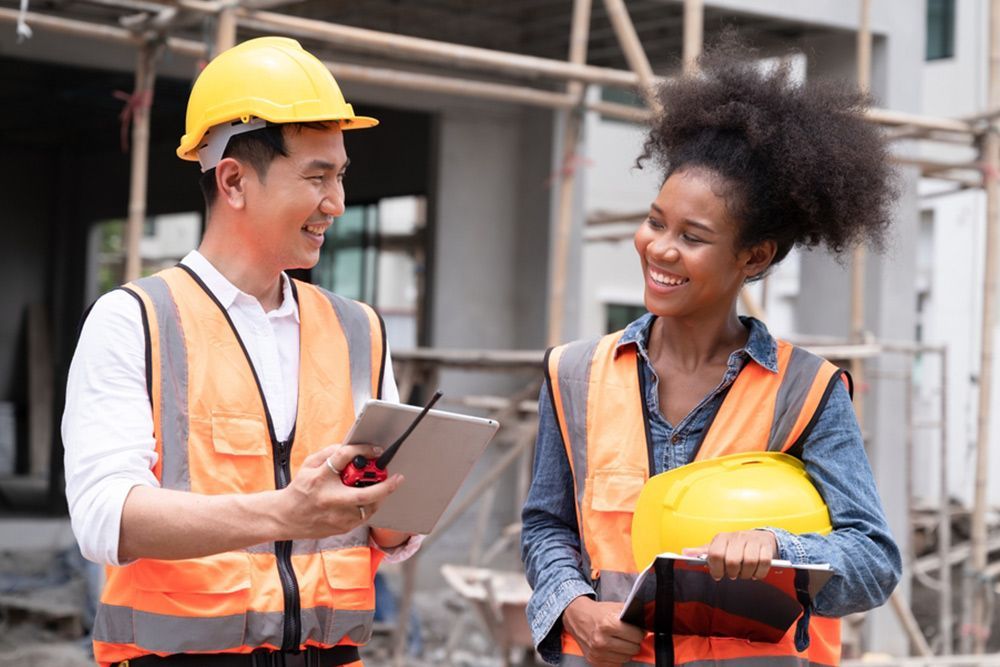 2 Worker Smiling Together While Holding a Notebook and Radio Phone — Builder in Rosedale, QLD