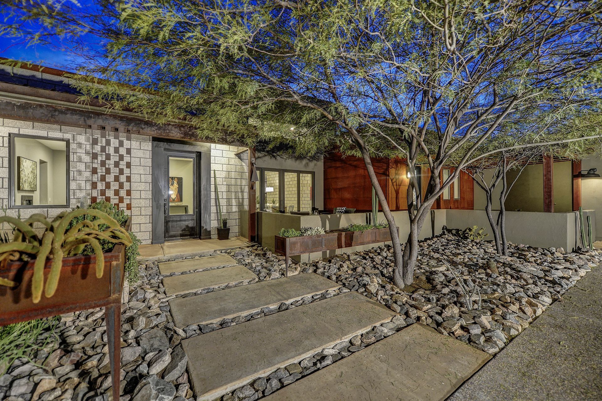 A house with a stone walkway leading to it and a tree in front of it.