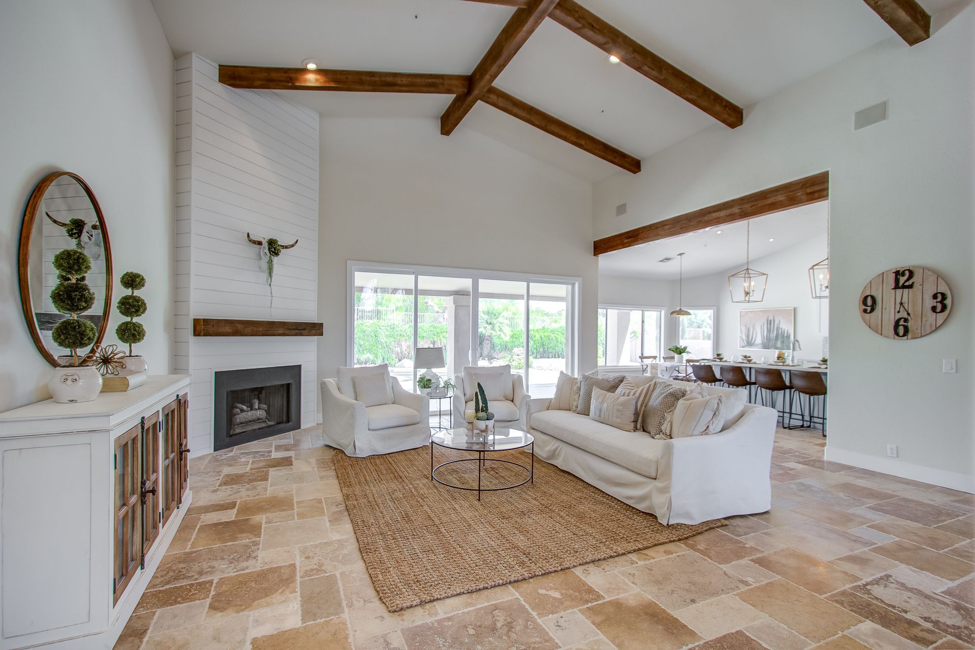 A living room with a couch , chairs , a fireplace and a clock on the wall.