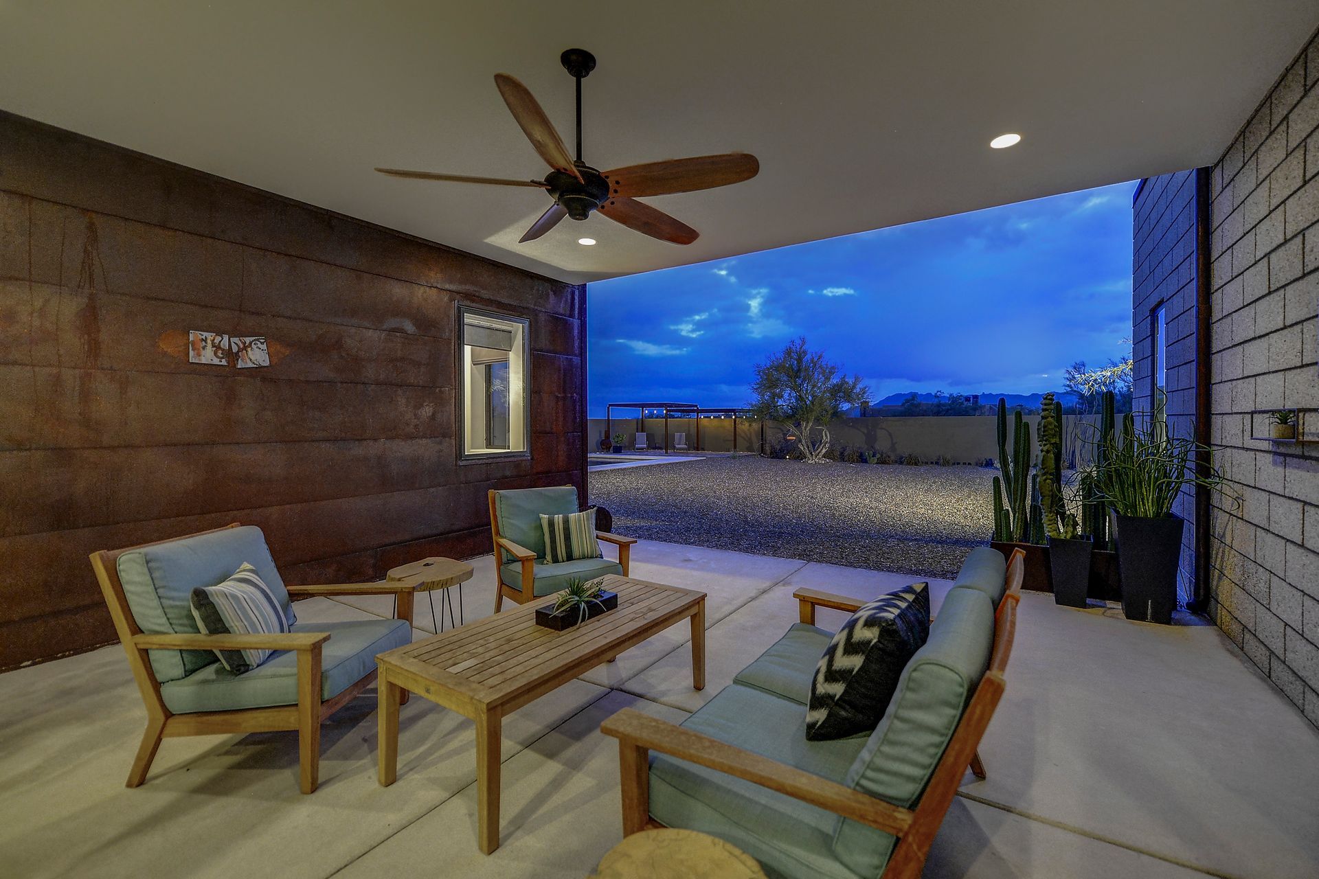 A patio with a couch , chairs , coffee table and ceiling fan.