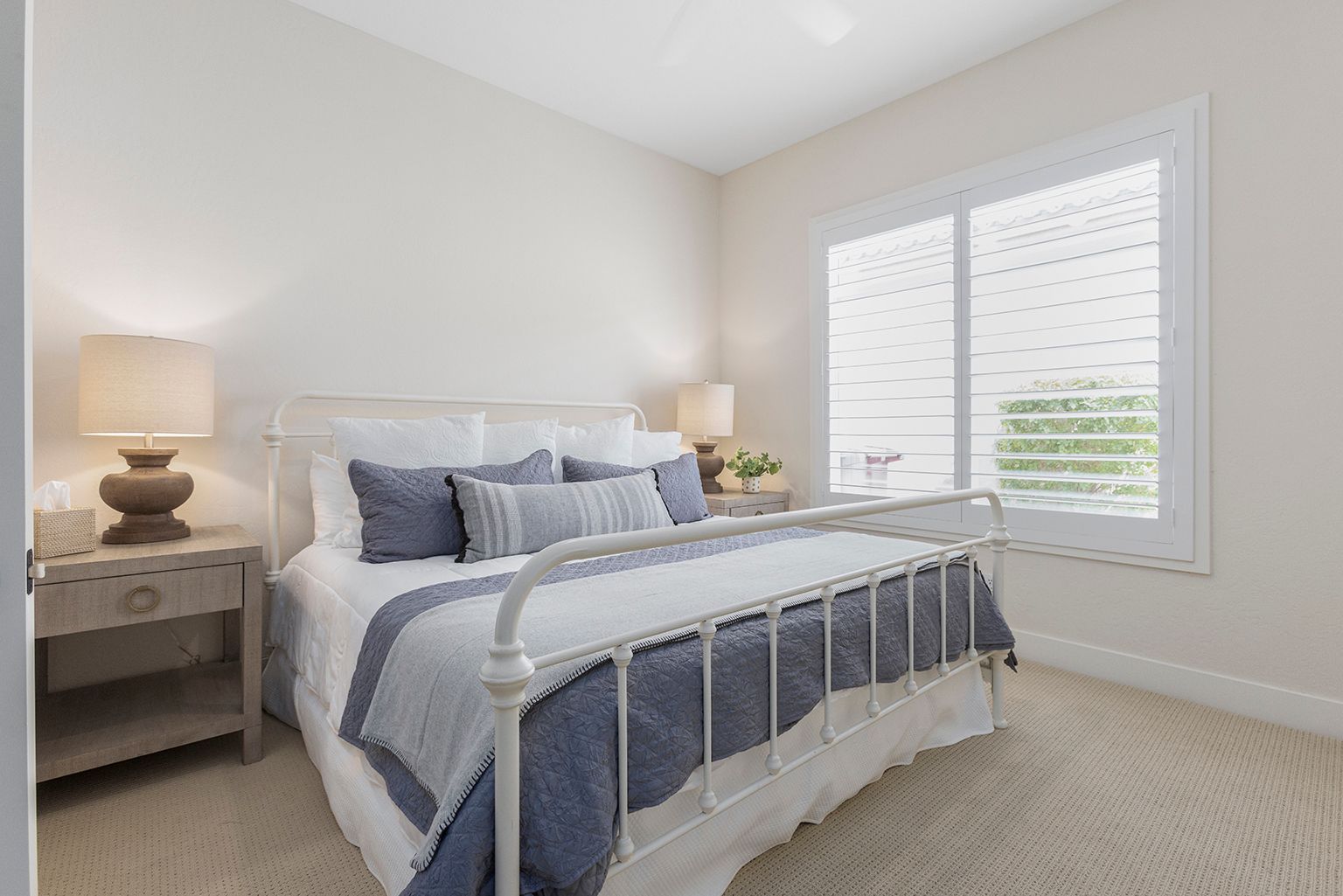 A bedroom with a bed , nightstand , lamp and window.