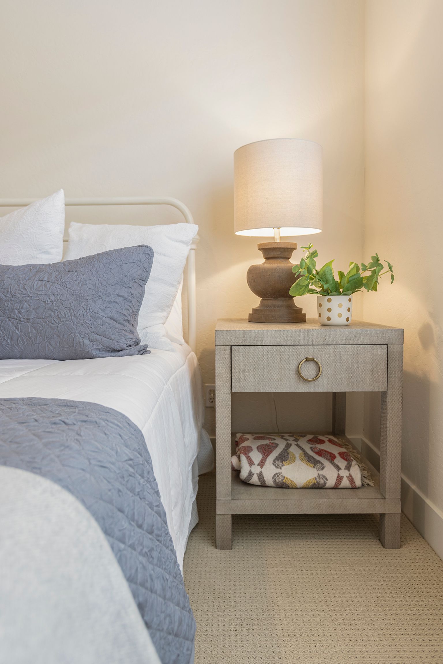 A bedroom with a bed , nightstand , lamp and plant.