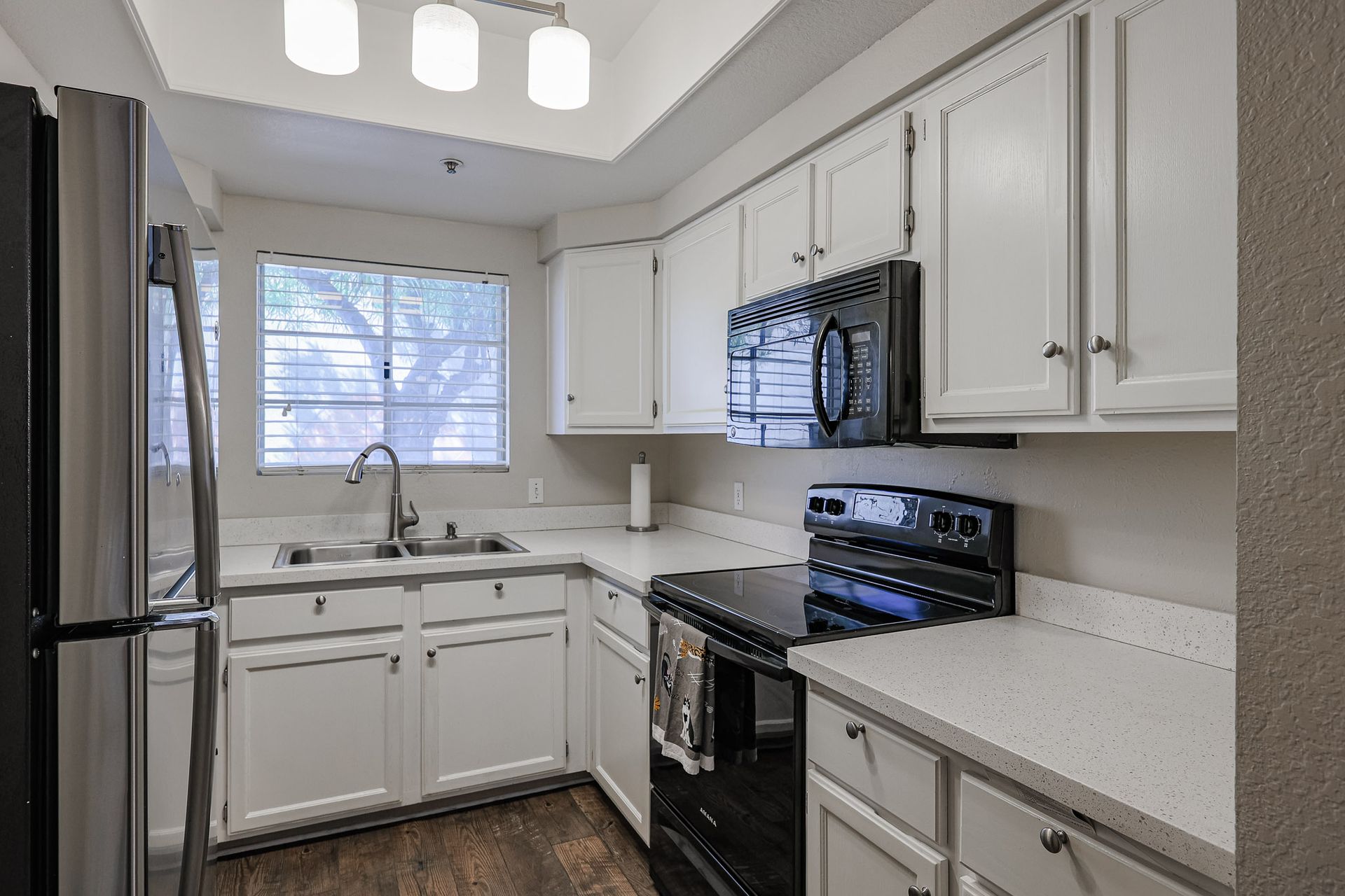 A kitchen with white cabinets , stainless steel appliances , a stove , microwave and refrigerator.
