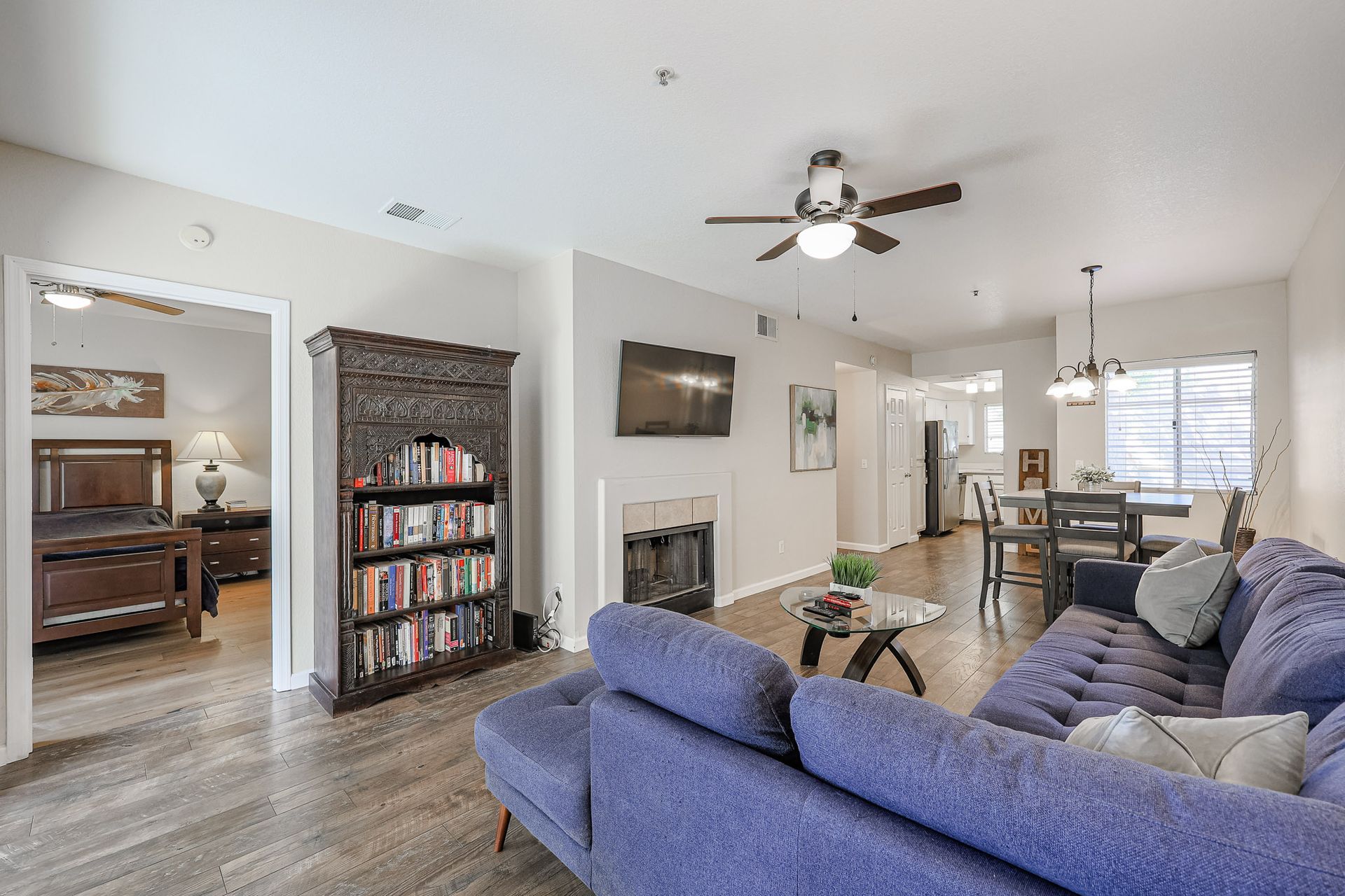 A living room with a purple couch , bookshelf , fireplace and ceiling fan.