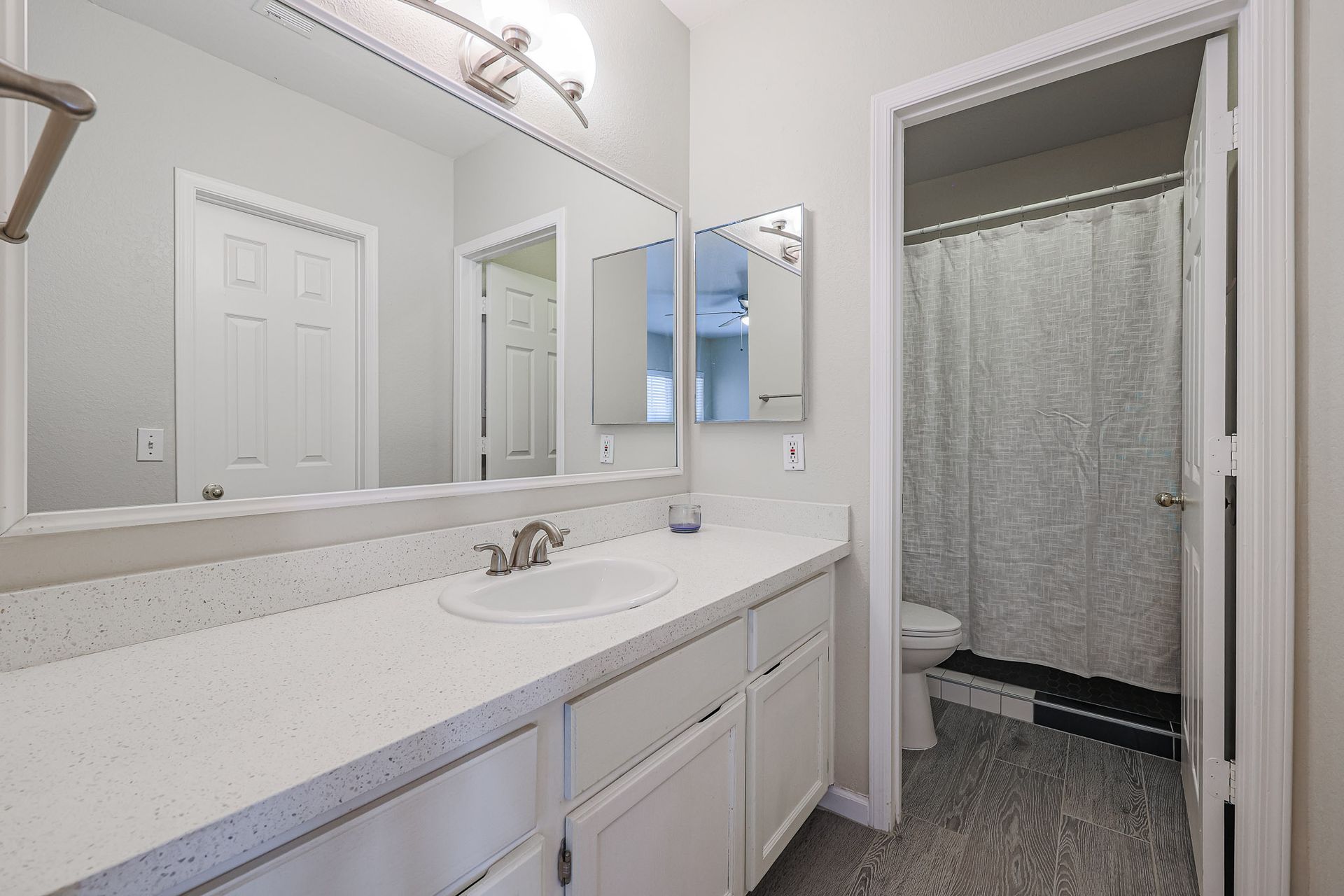 A bathroom with a sink , mirror , toilet and shower.