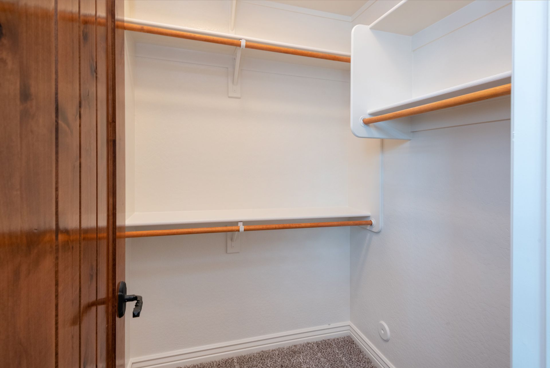 An empty walk in closet with wooden shelves and a wooden door.