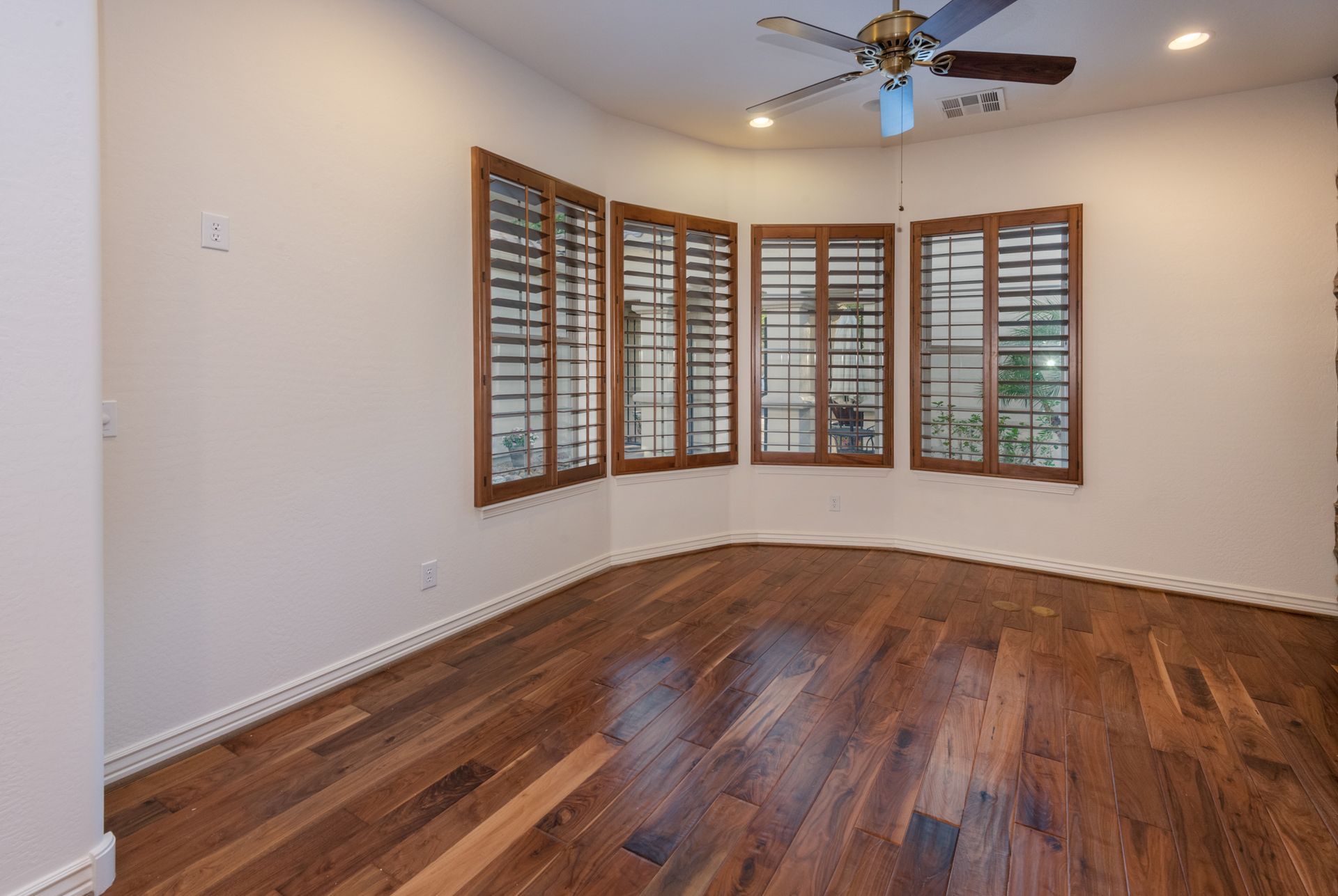 An empty room with hardwood floors and a ceiling fan.