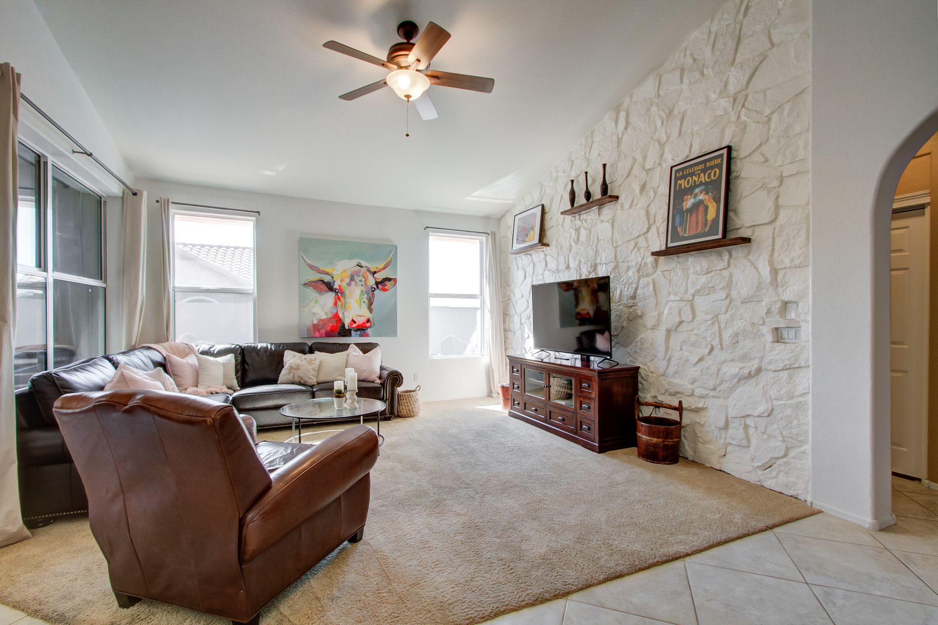 A living room with a couch , chair , television and ceiling fan.