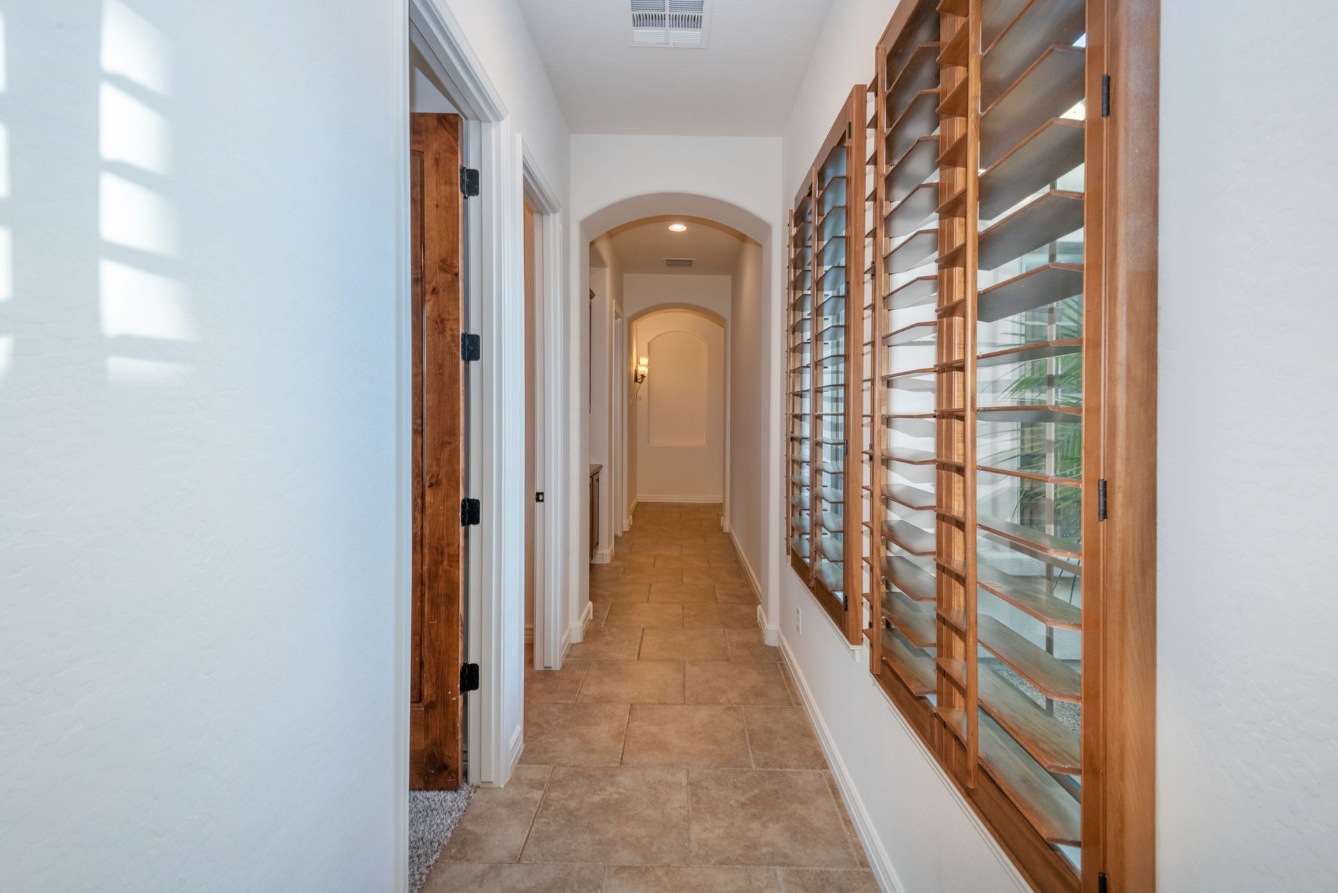 A long hallway in a house with shutters on the windows.
