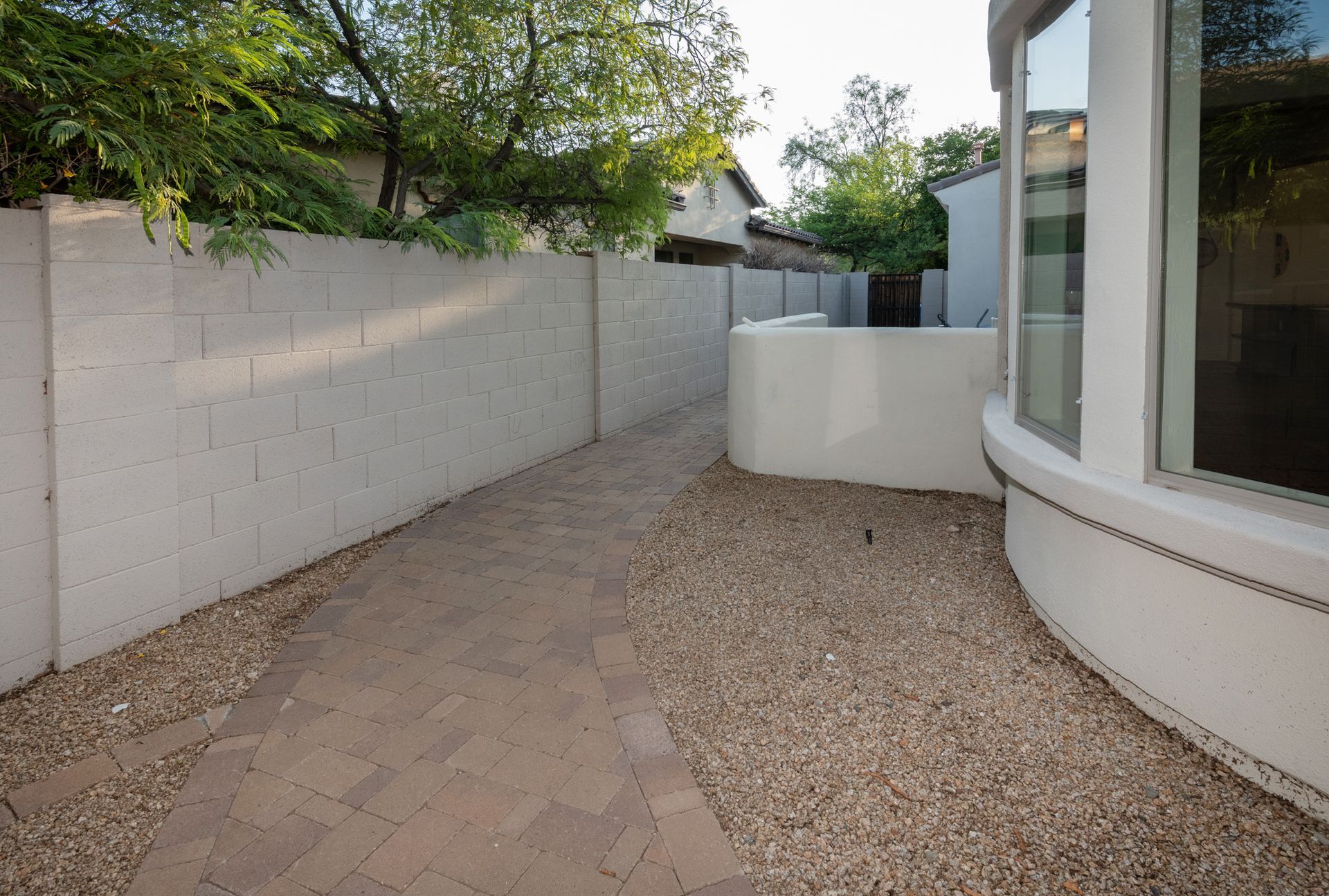 A brick walkway leading to a house with a white fence