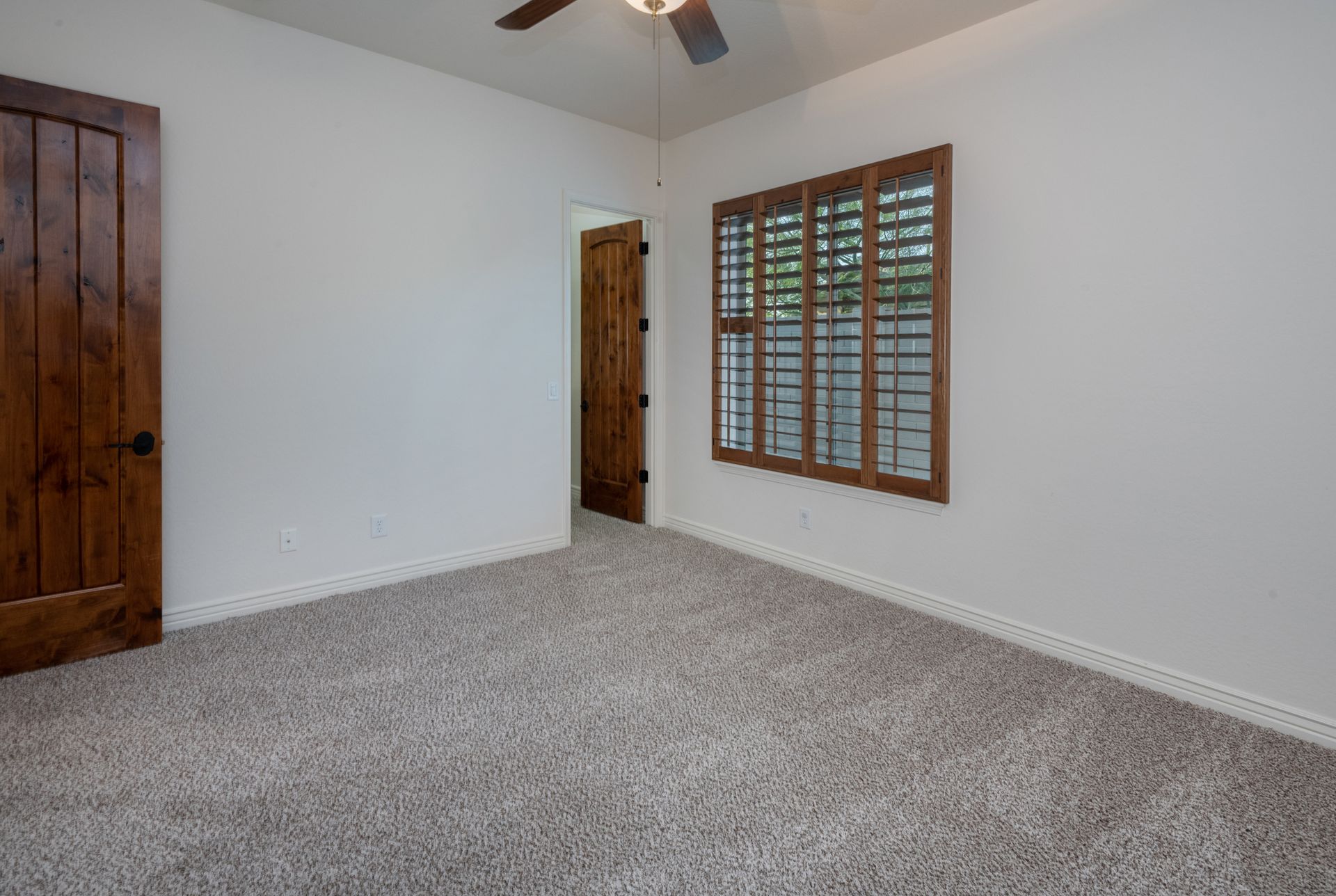 An empty bedroom with a ceiling fan and shutters on the windows.